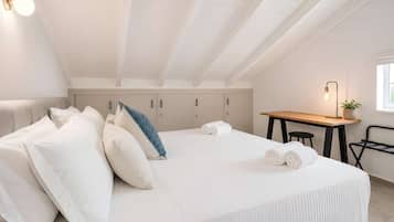 A bedroom with a bed, pillows, a desk, a chair, and a lamp.