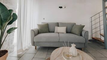 A modern living room with a grey sofa, a round table with a white vase, and a large plant.