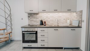 A modern kitchen with white cabinets, a built-in oven, a sink, and a tiled backsplash. - Luminis Residence by All about Paxos (Gaios)