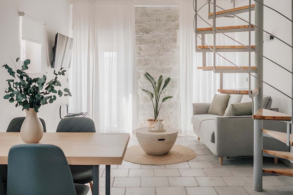 A modern living room with a staircase, a dining area with a table and chairs, and a large potted plant.