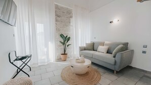 A modern living room with a grey sofa, a round coffee table, a potted plant, and a woven pouf. - Luminis Residence by All about Paxos (Gaios)