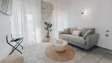 A modern living room with a grey sofa, a round coffee table, a potted plant, and a woven pouf.