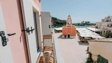 A balcony with a view of a coastal town, a building with a bell tower, and a paved area with umbrellas.