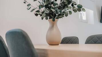 A dining table with a vase of green foliage, two upholstered chairs, and a plain wall in the background.