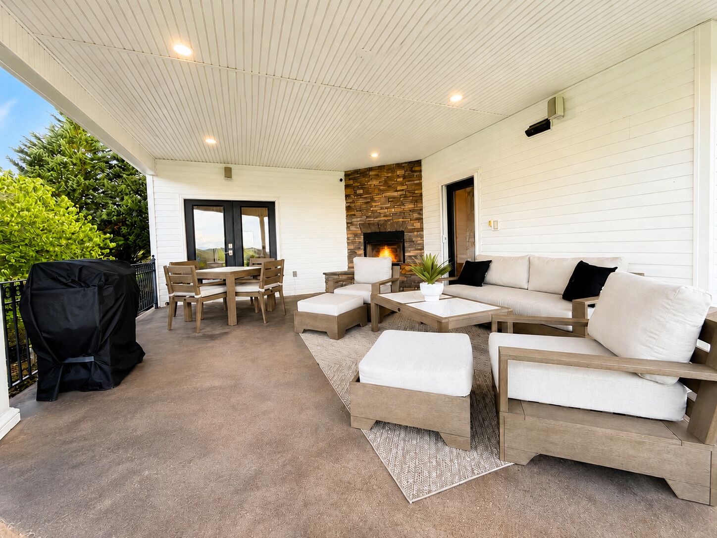 Un patio couvert avec une cheminée en pierre, des meubles d’extérieur et un barbecue.
