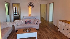 A living room with a sofa, a coffee table, a chandelier, and a clock on the wall. - Fully renovated apartment in the heart of Propriano (Propriano)