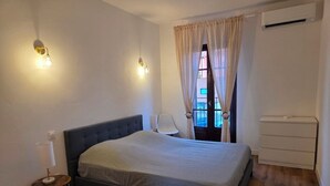 A bedroom with a bed, bedside lamp, air conditioning unit, and a window with curtains. - Fully renovated apartment in the heart of Propriano (Propriano)
