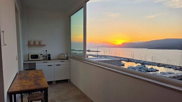 A balcony with a view of a sunset over water, a small kitchen area, and a wooden table. - Fully renovated apartment in the heart of Propriano (Propriano)