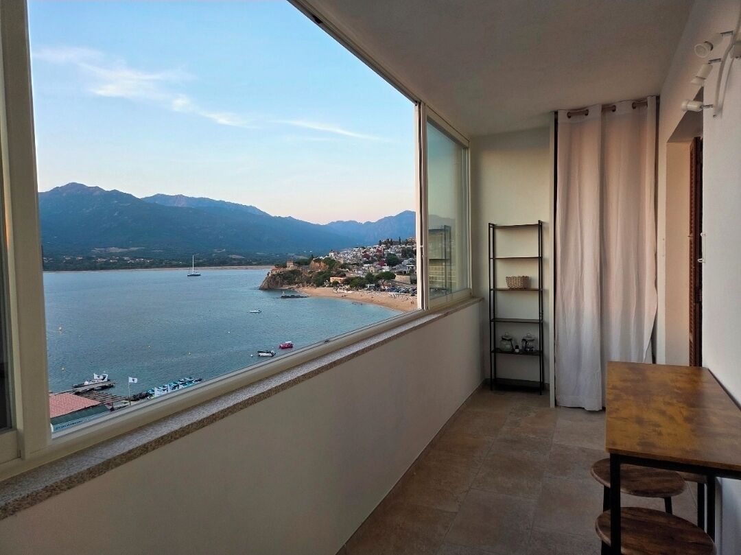 A balcony with a view of a body of water, a mountain range, and a distant shoreline.