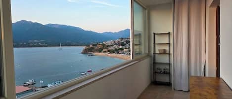 A balcony with a view of a body of water, a mountain range, and a distant shoreline.