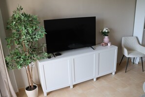 A living room with a flat-screen TV on a white cabinet, a potted plant, a white chair, and a small vase with flowers. - Apartment 'Casa Maje' with Shared Terrace and Wi-Fi (Fuente Álamo de Murcia)