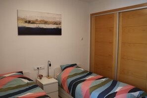 A bedroom with two beds, a bedside table with a lamp, a wooden wardrobe, and a painting on the wall. - Apartment 'Casa Maje' with Shared Terrace and Wi-Fi (Fuente Álamo de Murcia)