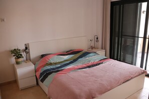 A bedroom with a bed, a bedside table with a lamp, a potted plant, and a window with blinds. - Apartment 'Casa Maje' with Shared Terrace and Wi-Fi (Fuente Álamo de Murcia)