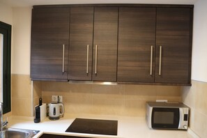A kitchen with dark wooden cabinets, a built-in microwave, a kettle, and an induction cooktop. - Apartment 'Casa Maje' with Shared Terrace and Wi-Fi (Fuente Álamo de Murcia)