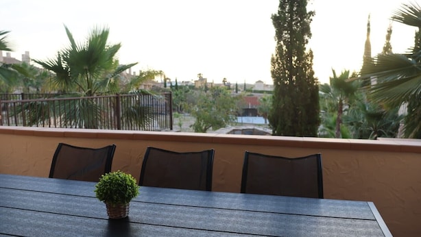 A balcony with a table and chairs, overlooking a residential area with trees and buildings.