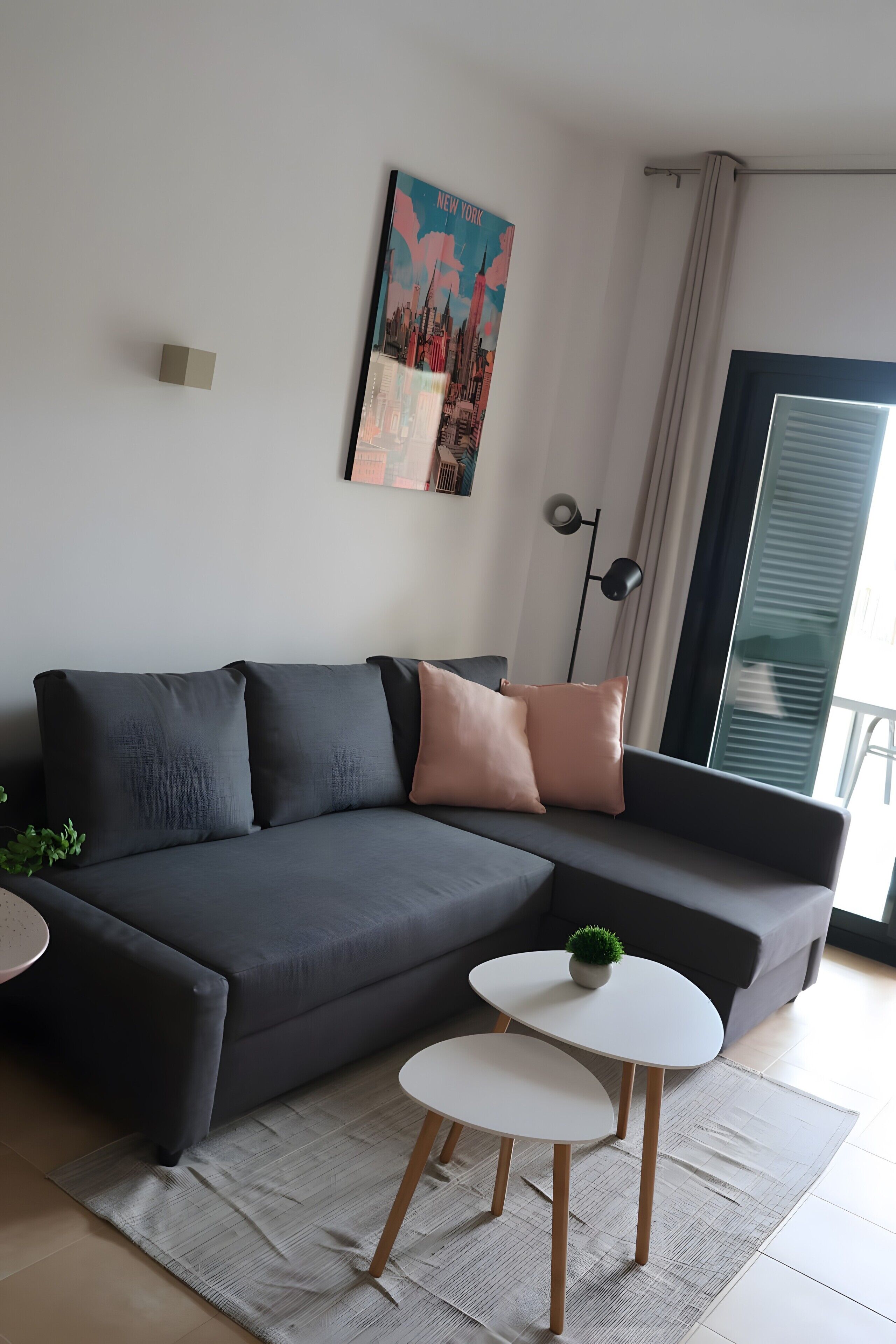 Ein modernes Wohnzimmer mit einem grauen Ecksofa, zwei weißen Beistelltischen, einer Stehlampe und einem Stadtplakat an der Wand.