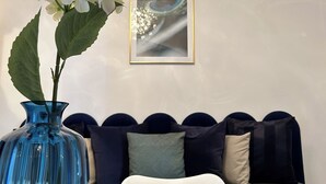 A room with a blue vase, a white cushion, and a framed picture on the wall.