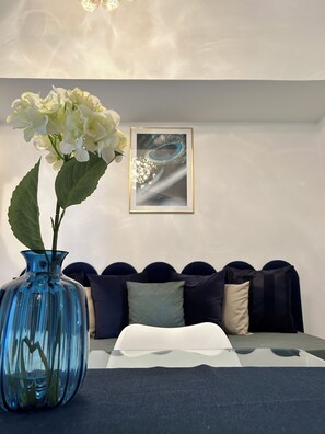 A room with a blue vase, a white cushion, and a framed picture on the wall.