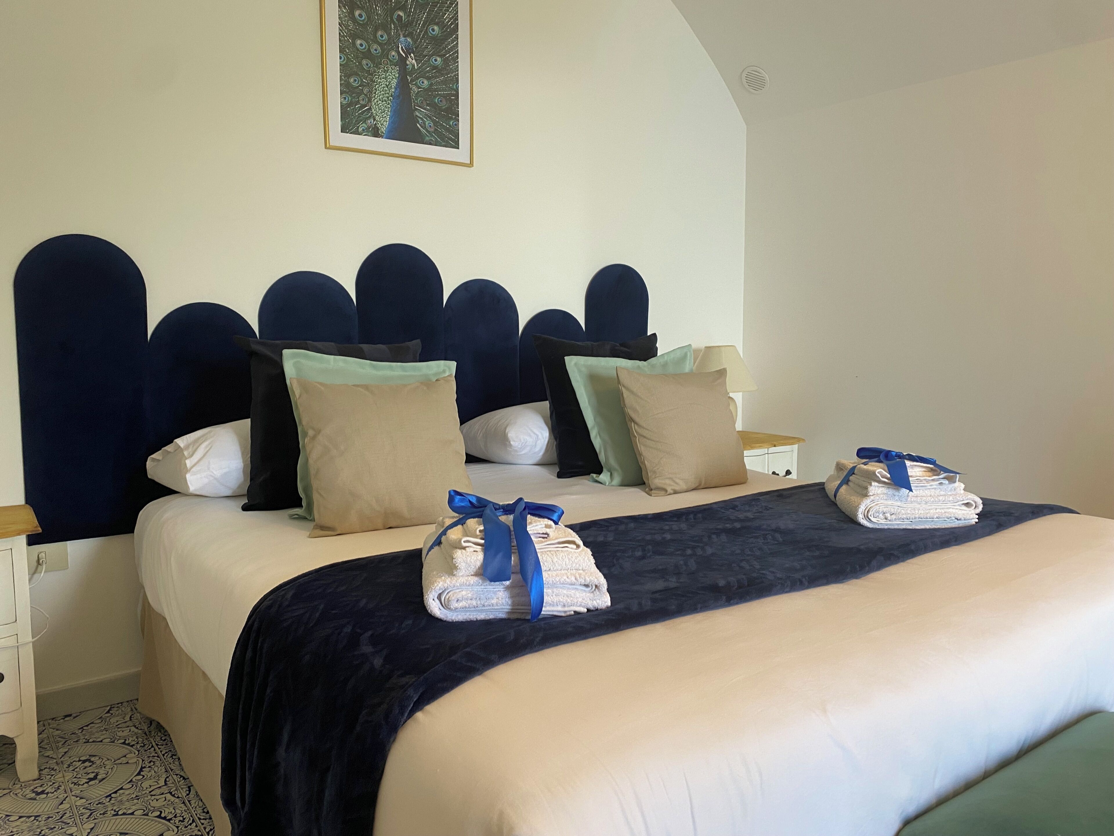 A neatly made bed with a dark headboard, multiple pillows, and folded towels on the side.