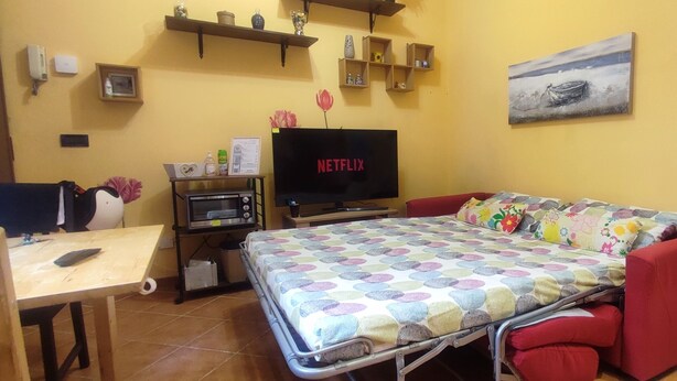 A small room with a bed, a TV, a desk, and shelves with various items. - Casa Vitto 1-Room Apartment, A/C, 8 min from the airport, 10 min from the beach by car or bus (Genova)