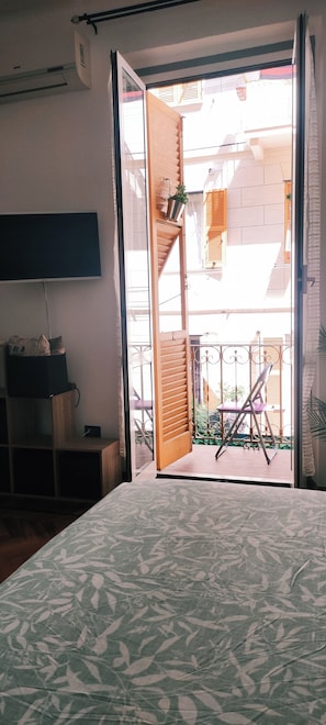 Ein Zimmer mit einem Bett, einem Schreibtisch und einer Glastür, die auf einen Außenbereich mit Balkon und Stuhl führt.