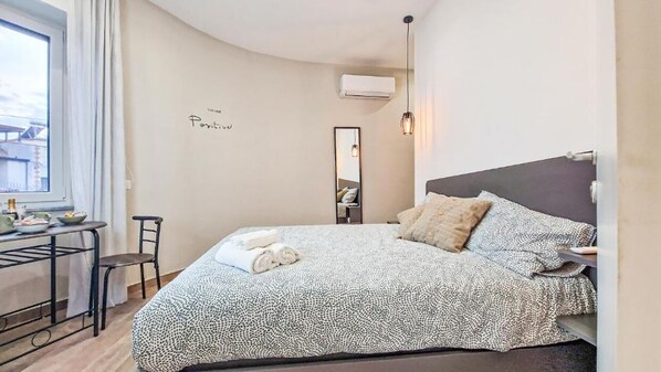 Habitación de hotel con cama, escritorio, silla, espejo y unidad de aire acondicionado.