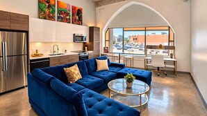 Ein modernes Wohnzimmer mit einer Eckcouch, einem Glastisch und Blick auf die Stadt durch große Fenster.