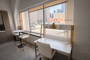 Um espaço de escritório moderno com mesas e cadeiras brancas, e uma grande janela com vista para a paisagem urbana.
