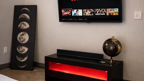 Ein Zimmer mit an der Wand montiertem Fernseher, der das Netflix-Logo zeigt, einer schwarzen Unterhaltungsanlage mit rot beleuchteten Elementen und einem Globus darauf.