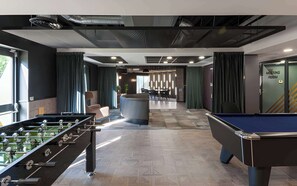 Ein moderner Indoor-Freizeitbereich mit Tischfußballtischen, einer Billardkugel und einer Bar.