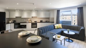 A modern kitchen with built-in appliances, a dining area with a table and chairs, a grey sofa, and a small round table with a plant. - Student Only New Park - Edinburgh (Edinburgh)
