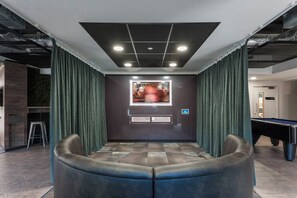 Ein Raum mit Billardtisch, einer Sitzecke mit gebogener Bank und einem an der Wand montierten Fernseher.