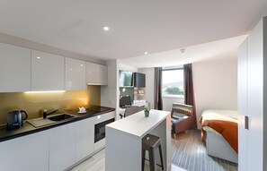 A modern hotel room with a kitchenette, a bed, a desk, and a view of the outdoors. - Student Only New Park - Edinburgh (Edinburgh)