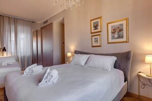 A hotel room with a large bed, two bedside tables, a wardrobe, and a chandelier. - Luxury Riverside Apartment with Arno Views, Balconies & Private Garage (Firenze)