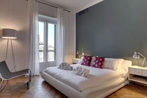 A modern hotel room with a large bed, a chair, a desk, and a window with curtains. - Luxury Riverside Apartment with Arno Views, Balconies & Private Garage (Firenze)