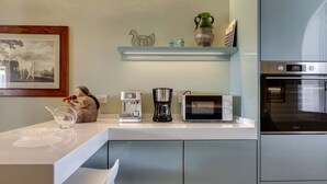 Eine moderne Küche mit weißer Arbeitsplatte, einer Kaffeemaschine, einer Mikrowelle und einem Backofen.