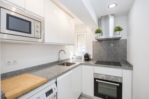 A modern kitchen with white cabinets, a granite countertop, a built-in microwave, a stainless steel range hood, and a dishwasher. - GuestReady - Triana Tadeo Soler Sevilla (Sevilla)