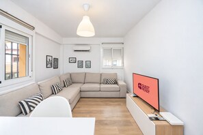 A modern living room with a beige sofa, a flat-screen TV, and a wooden desk. - GuestReady - Modern escape in Sevilla (Sevilla)