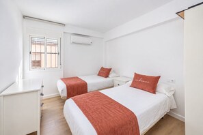 Une chambre d’hôtel avec deux lits, une fenêtre, un appareil de climatisation et un bureau blanc.