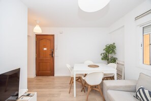 A modern living room with a white table, chairs, a sofa, a TV, and a wooden door. - GuestReady - Triana Tadeo Soler Sevilla (Sevilla)