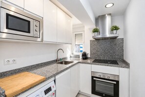 A modern kitchen with white cabinets, a stainless steel microwave, a built-in oven, a granite countertop, and a stainless steel range hood. - GuestReady - Modern escape in Sevilla (Sevilla)