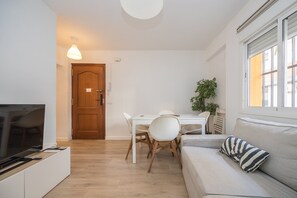 A living room with a TV, a dining table with chairs, a sofa, and a window. - GuestReady - Triana Tadeo Soler Sevilla (Sevilla)