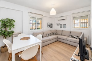 Un salon moderne avec un canapé blanc, une table à manger avec des chaises, une plante en pot et un téléviseur.