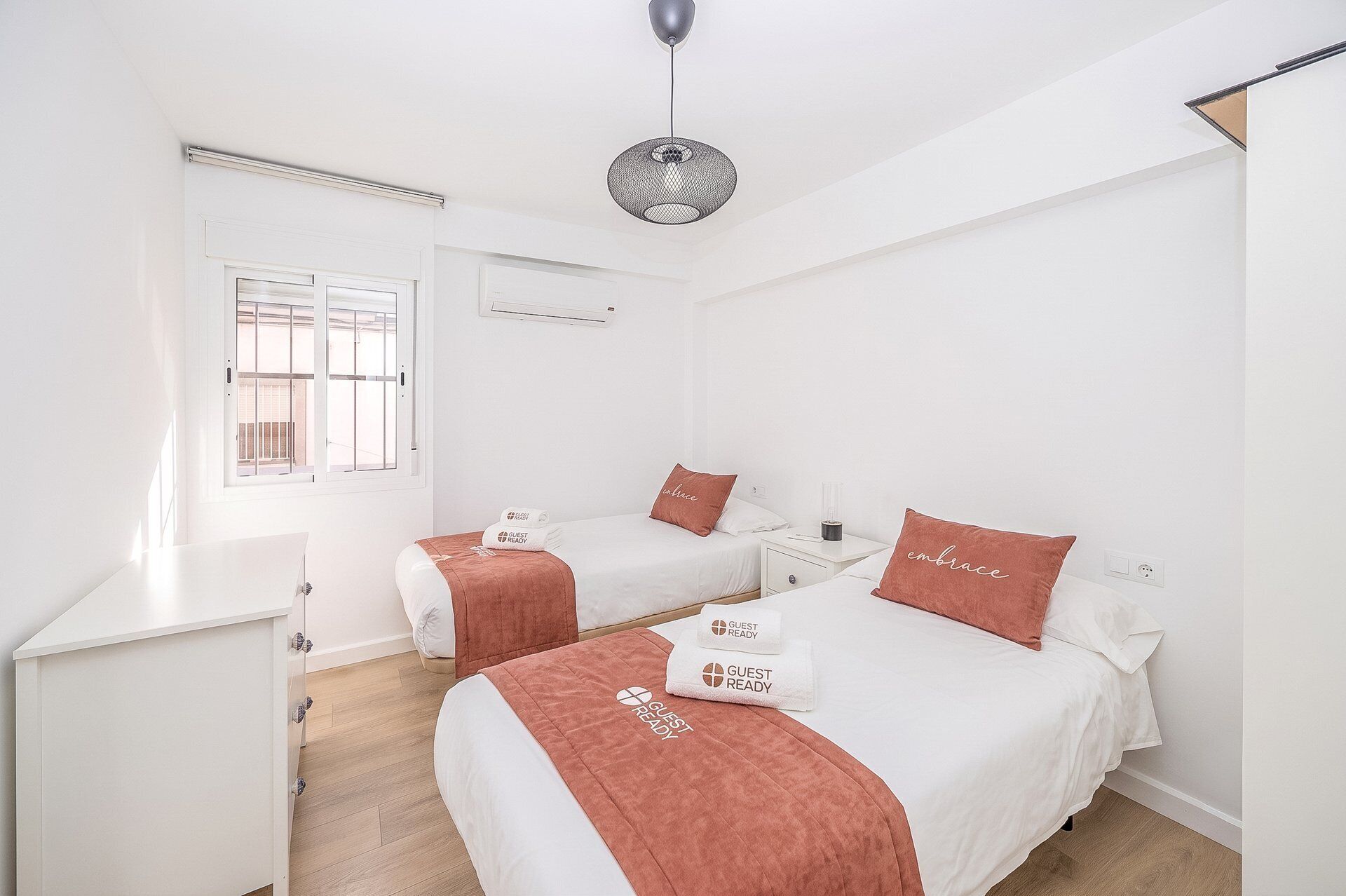 Een hotelkamer met twee bedden, een bureau, een raam en een hanglamp.