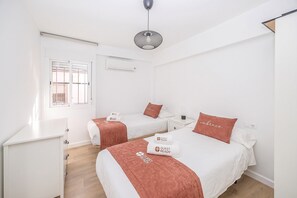 A hotel room with two beds, a desk, a window, and a hanging light fixture. - GuestReady - Triana Tadeo Soler Sevilla (Sevilla)