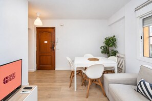 A modern living room with a sofa, a dining table with chairs, a television, and a wooden door. - GuestReady - Modern escape in Sevilla (Sevilla)