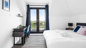 Ein modernes Hotelzimmer mit Bett, Schreibtisch, Stuhl und Blick durch eine Glastür.