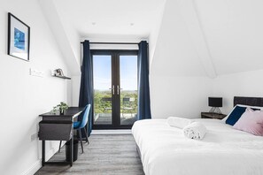 A modern hotel room with a bed, desk, chair, and a view through a glass door. - Panoramic View by MyCityHaven (Redland)