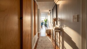 Un couloir avec des portes en bois, un tapis, un luminaire fixé au mur et une plante.