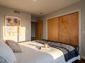 Ein Schlafzimmer mit einem Bett, einem großen Kleiderschrank und einem gerahmten abstrakten Gemälde an der Wand.